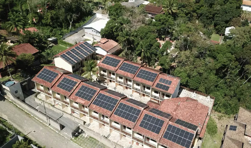 Vista aérea de um hotel em Ilhabela/SP com painéis solares sobre os telhados de telha cerâmica, cercado de mata